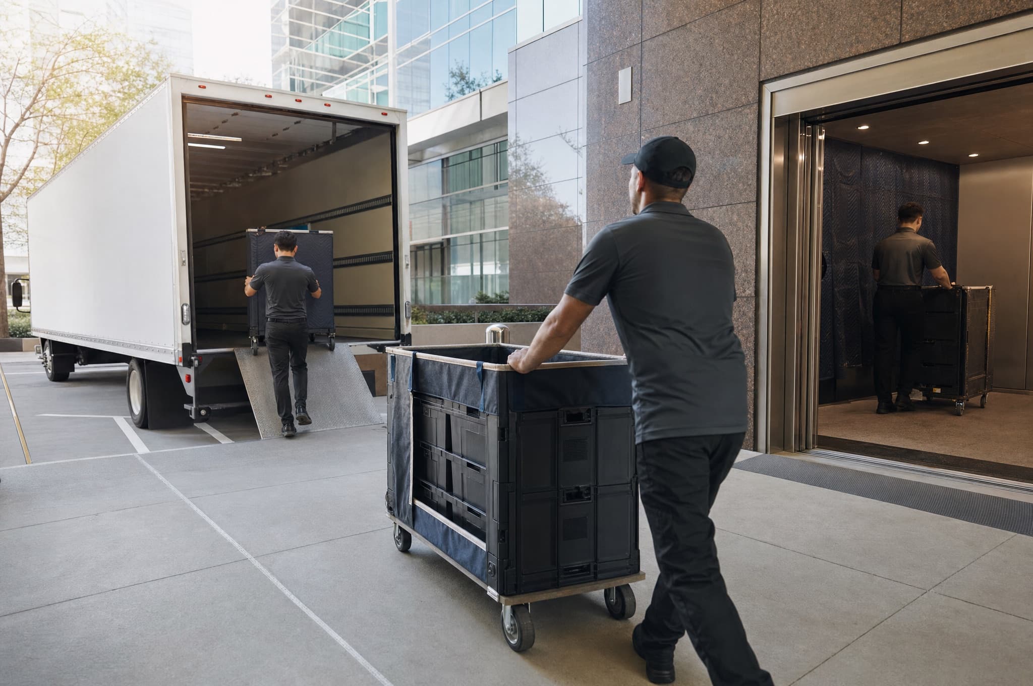 Movers wheeling library carts and office crates through the loading dock of a modern glass office building in Newport Center